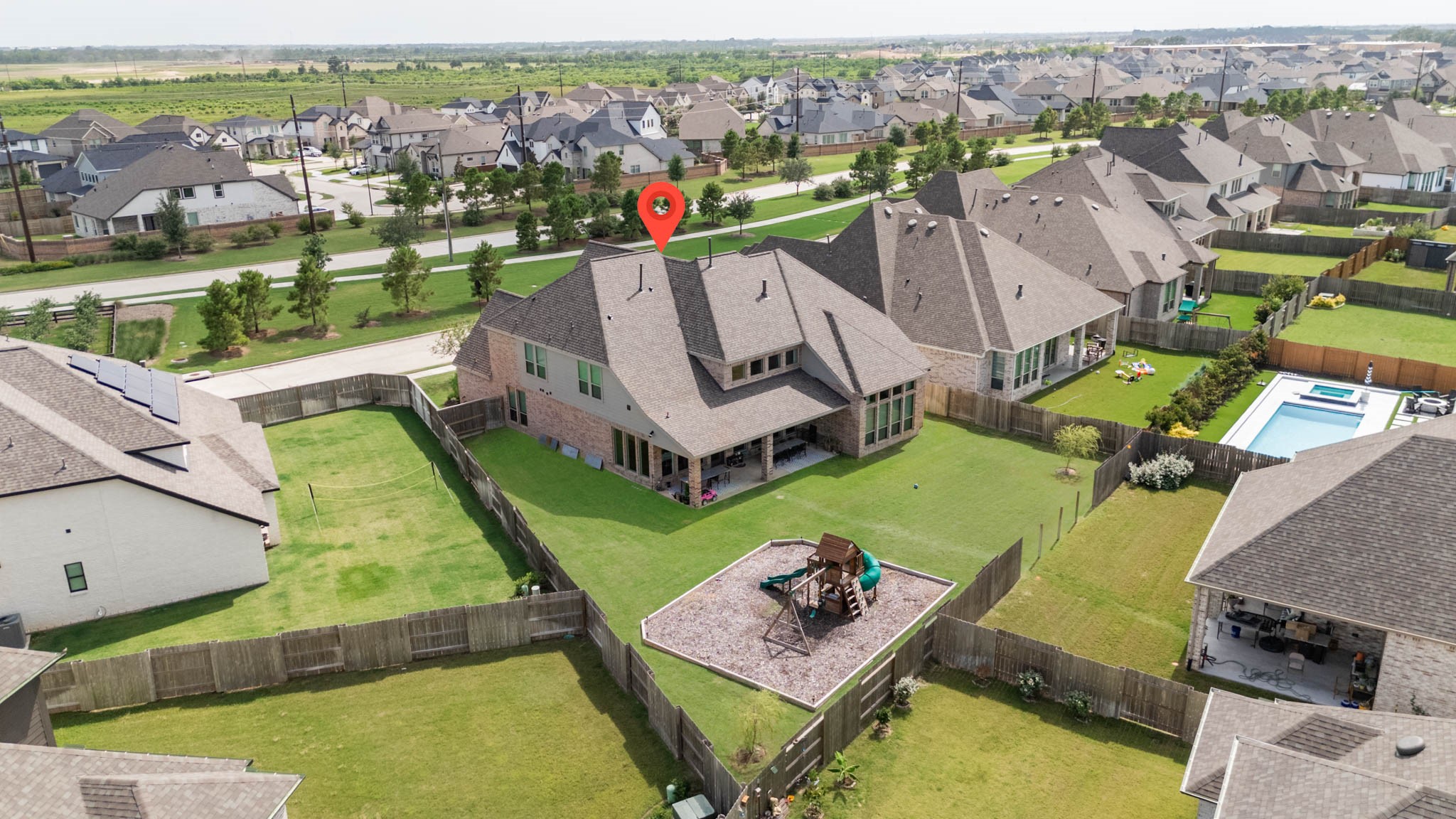 24430 Switchgrass Vly Way Katy, TX 77493 - Photo 50 of 50 This aerial photo showcases a spacious, fenced backyard with a playset, offering a large lawn area. The home features a modern roof design, and the neighborhood is filled with similar, well-maintained houses, indicating a vibrant community.