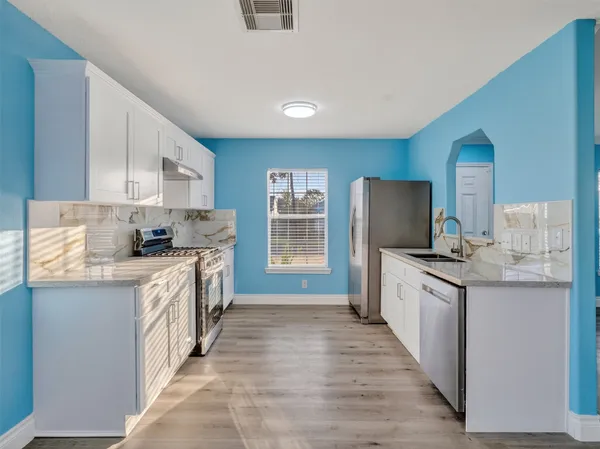 a kitchen with stainless steel appliances granite countertop a stove top oven a sink dishwasher a refrigerator and a oven with wooden floor