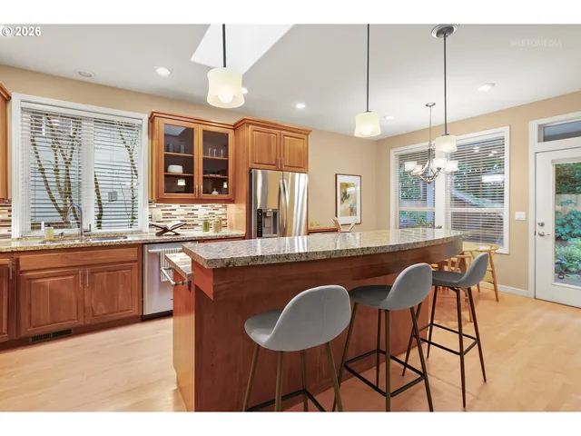 a open kitchen with granite countertop a stove a sink a kitchen island with chairs and wooden cabinets