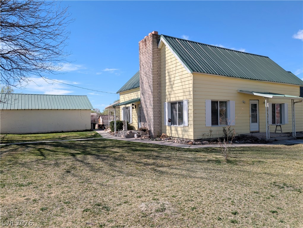 Back of property with a metal roof, a yard, and a chimney