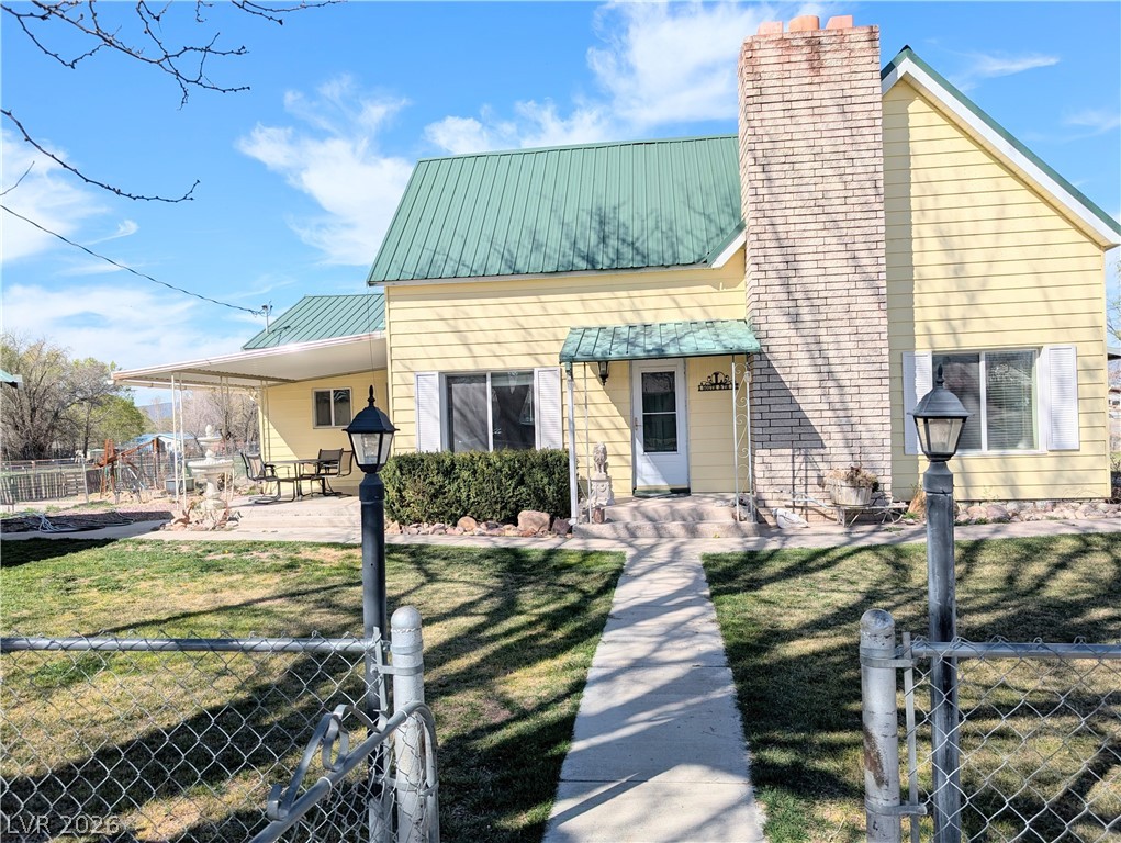 1 South 5th Street Panaca, NV 89042 - Photo 2 of 21 View of front of home with a fenced front yard, a metal roof, a chimney, and a gate