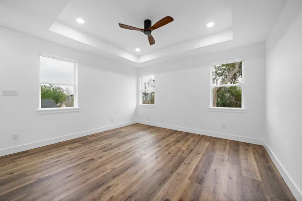an empty room with wooden floor ceiling fan and windows