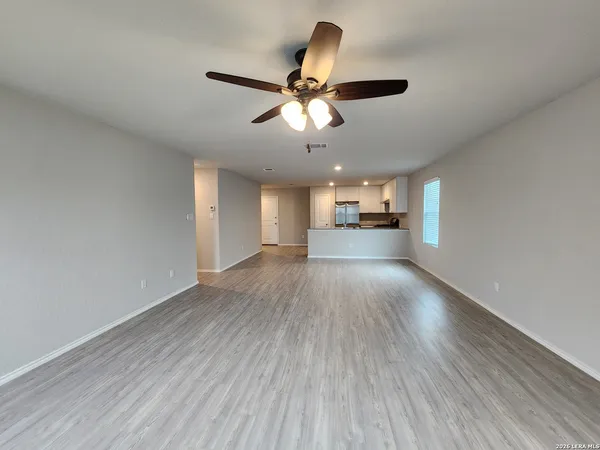 a view of a big room with wooden floor a ceiling fan and windows