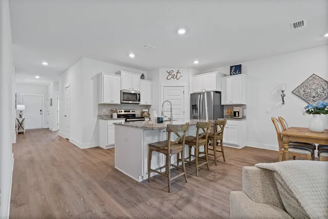 a kitchen with stainless steel appliances granite countertop a refrigerator a stove top oven a sink dishwasher and white cabinets with wooden floor
