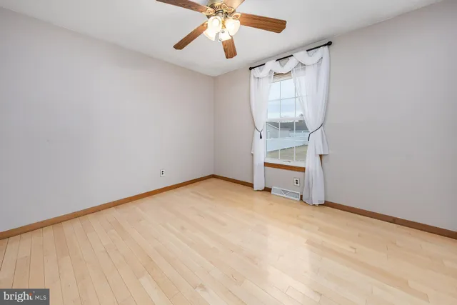 an empty room with chandelier fan and windows