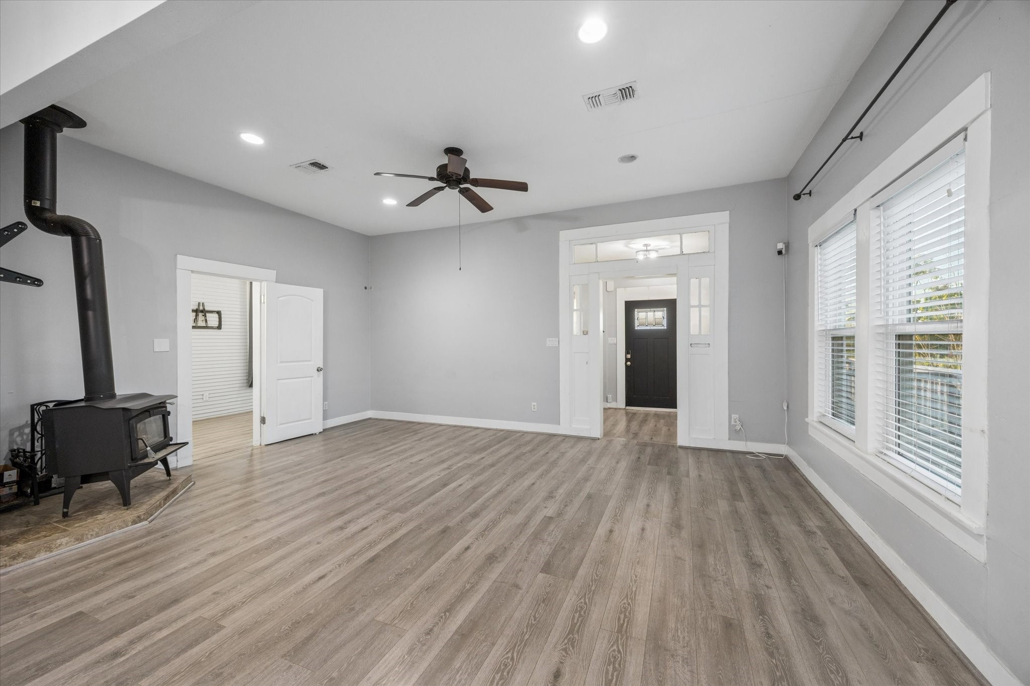 10347 Pless Road Cat Spring, TX 78933 - Photo 6 of 41 This spacious living area features wood flooring, a ceiling fan, and ample natural light from large windows. It includes a cozy wood-burning stove and provides access to adjacent rooms through white-framed doors.