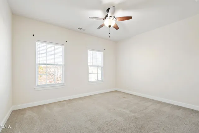 an empty room with chandelier fan and windows