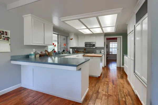 a kitchen with stainless steel appliances granite countertop wooden cabinets a refrigerator a sink a stove a microwave and wooden floors