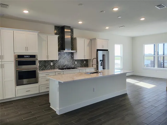 a large kitchen with stainless steel appliances granite countertop a stove a sink and a granite counter tops with wooden floors