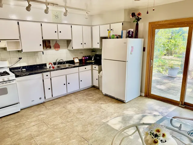 a kitchen with granite countertop a refrigerator a sink and white cabinets