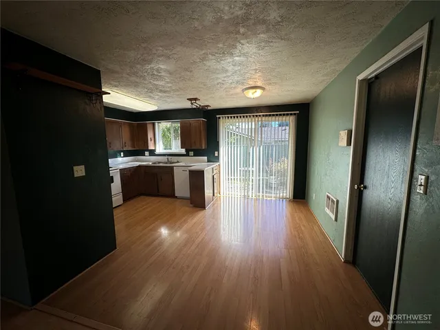 an empty room with wooden floor and a kitchen