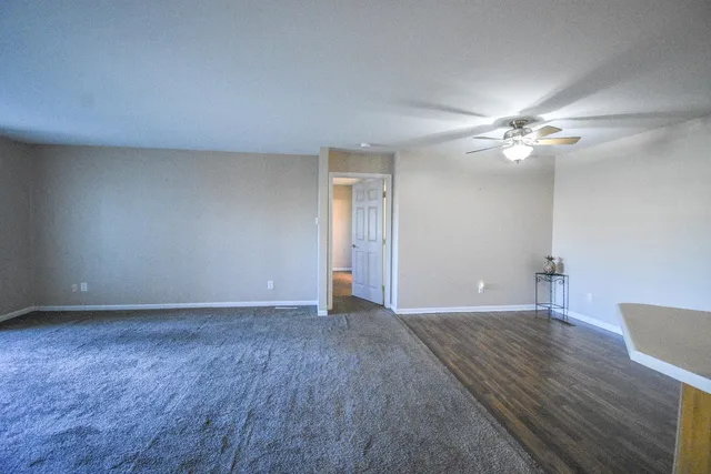a view of an empty room with chandelier fan and wooden floor