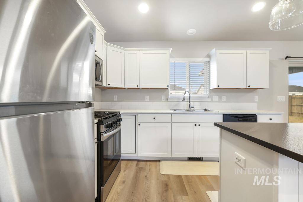 1113 Meadow Lake Loop Buhl, ID 83316 - Photo 23 of 27 Kitchen featuring stainless steel appliances, white cabinetry, light wood-type flooring, and pendant lighting