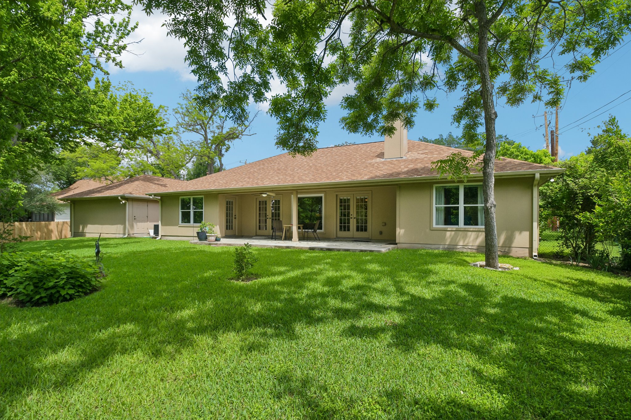 307 West 4th Street Elgin, TX 78621 - Photo 35 of 40 Expansive rear yard featuring a large patio, lush green lawn, mature trees, and a tan stucco exterior with multiple windows and French doors