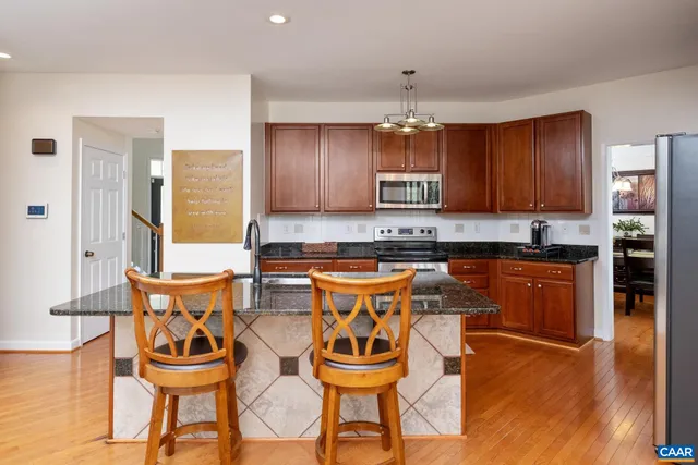 a kitchen with stainless steel appliances granite countertop a stove top oven a refrigerator a sink and dining table with wooden floor