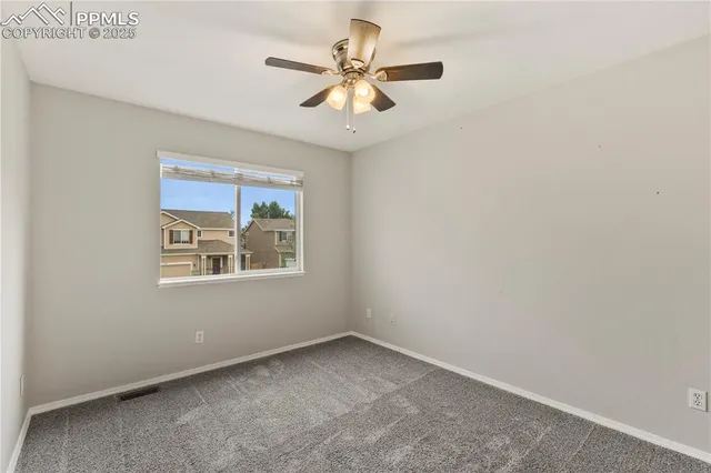 an empty room with chandelier fan and windows