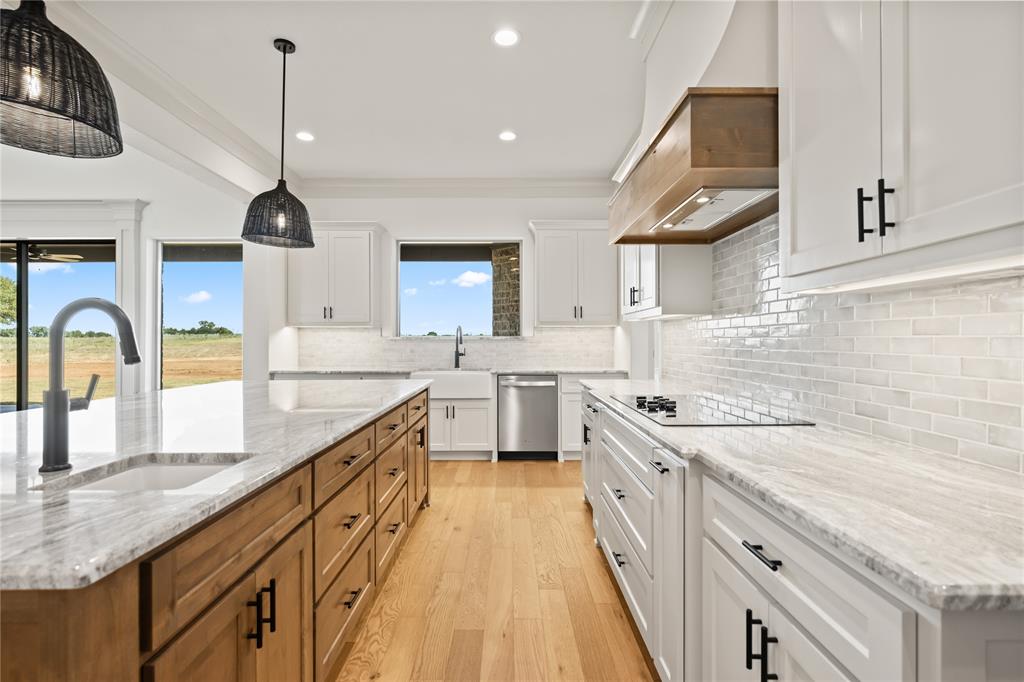 115 Red Bud Road Boyd, TX 76023 - Photo 17 of 38 Gourmet kitchen featuring a wood-finish island with integrated sink, light wood-finish flooring, white cabinetry with matte black hardware, stone countertops, and a subway tile backsplash