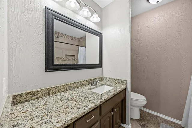 a bathroom with a granite countertop sink and a toilet