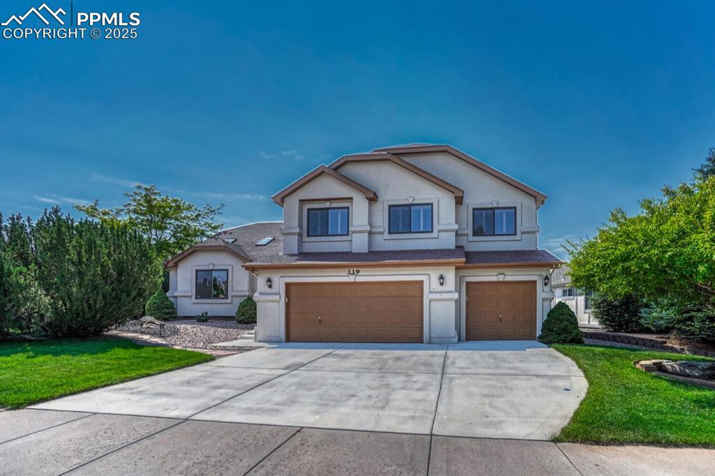 Traditional-style house featuring concrete driveway, an attached garage, stucco siding, and a front lawn