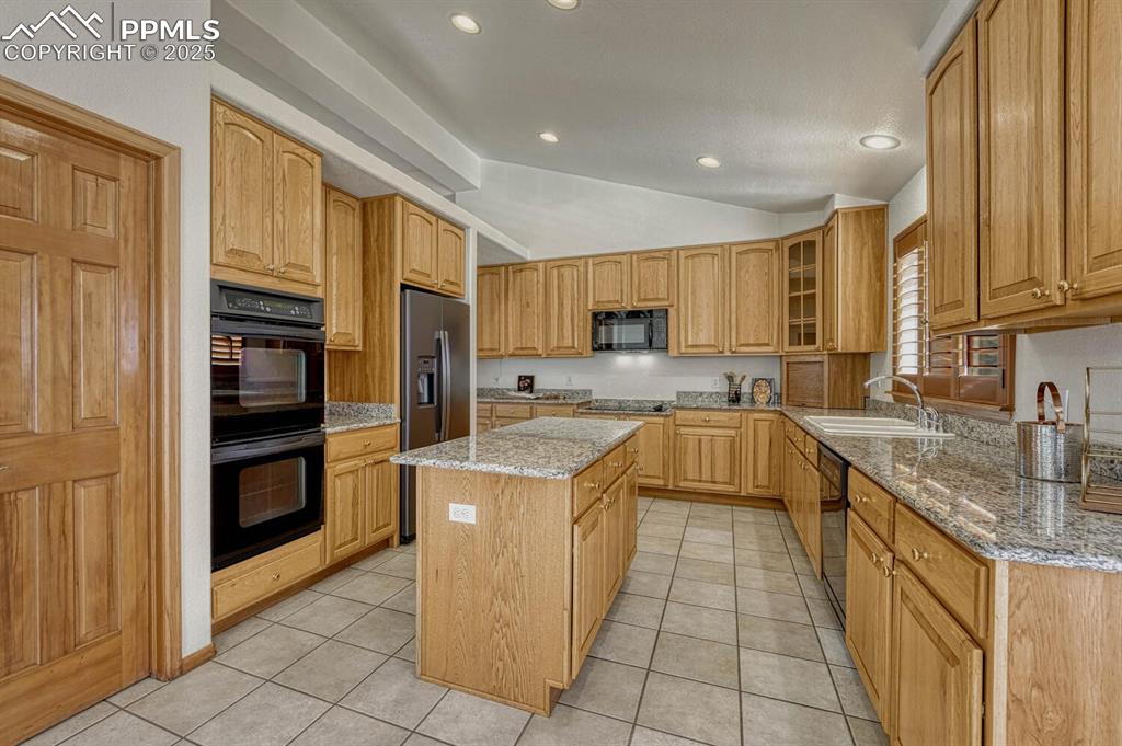 339 Sandreed Place Colorado Springs, CO 80921 - Photo 12 of 50 Kitchen featuring light stone countertops, black appliances, vaulted ceiling, a kitchen island, and glass insert cabinets