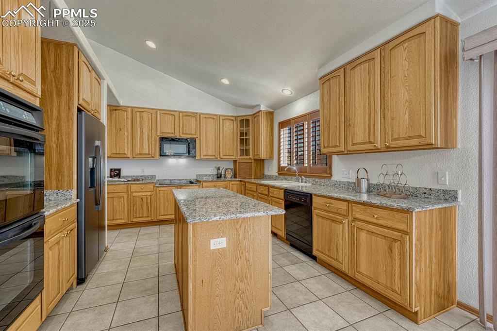 339 Sandreed Place Colorado Springs, CO 80921 - Photo 13 of 50 Kitchen with light stone counters, black appliances, lofted ceiling, light tile patterned flooring, and glass insert cabinets