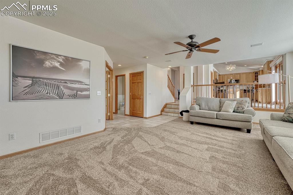 339 Sandreed Place Colorado Springs, CO 80921 - Photo 18 of 50 Living room featuring light carpet, a chandelier, stairway, a textured ceiling, and a ceiling fan
