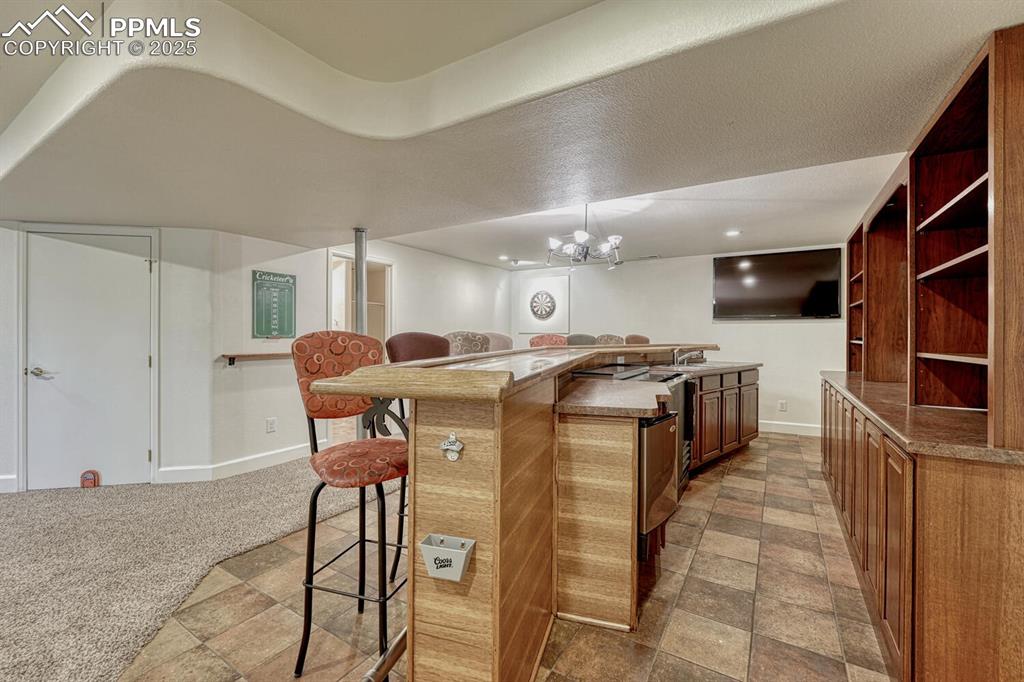 339 Sandreed Place Colorado Springs, CO 80921 - Photo 37 of 50 Kitchen featuring a breakfast bar area, an island with sink, open shelves, light stone finish flooring, and light colored carpet