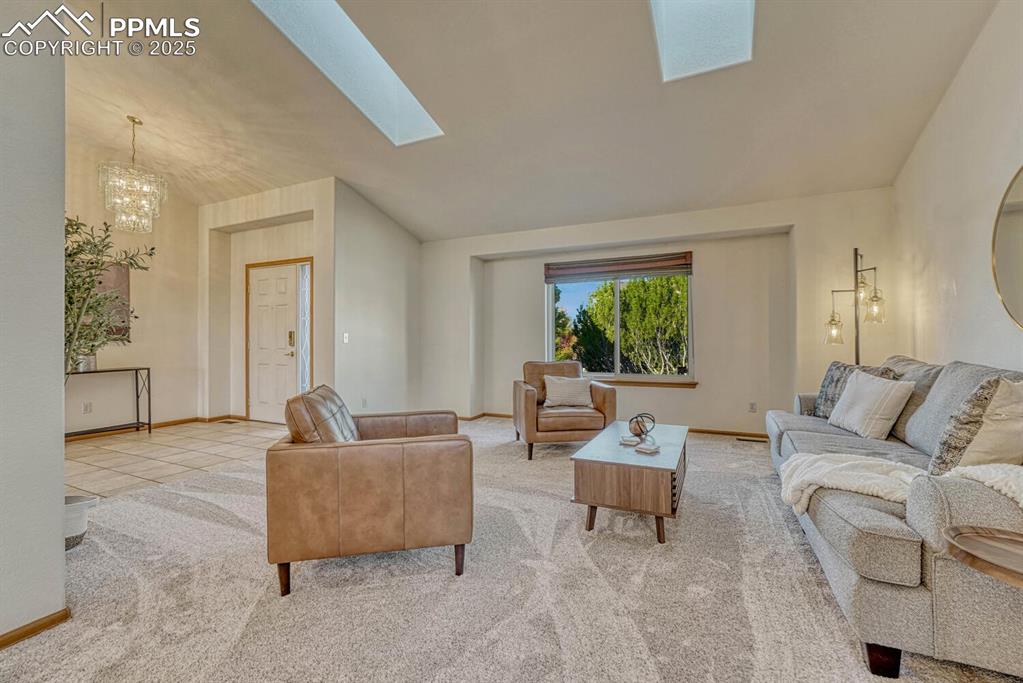 339 Sandreed Place Colorado Springs, CO 80921 - Photo 6 of 50 Carpeted living area featuring lofted ceiling, a chandelier, a skylight, and tile patterned floors