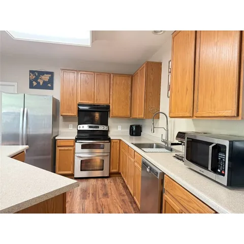 a kitchen with stainless steel appliances kitchen island granite countertop a stove a sink dishwasher and a refrigerator with wooden floor