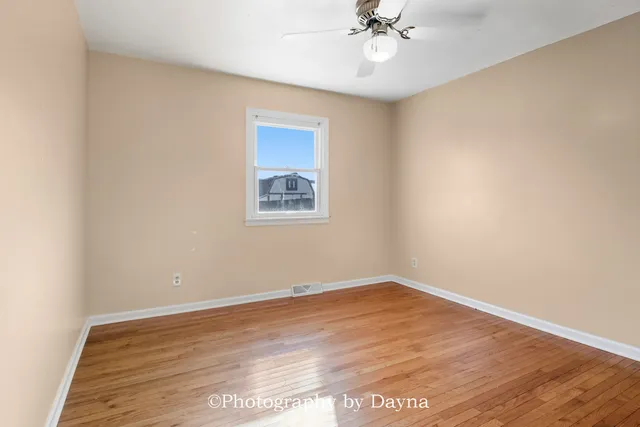 a view of an empty room with wooden floor and a fan