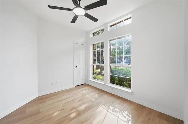 an empty room with wooden floor fan and windows