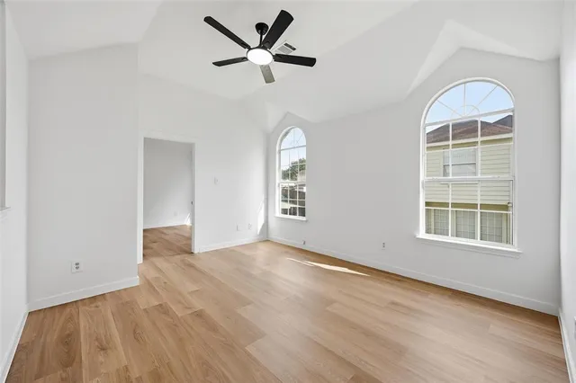 an empty room with wooden floor a ceiling fan and windows