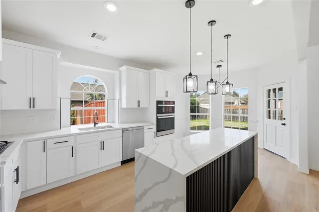 a room with stainless steel appliances kitchen island granite countertop a sink a stove and a wooden floors
