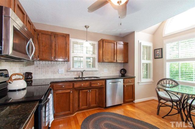 a kitchen with stainless steel appliances granite countertop a stove top oven a sink dishwasher a dining table and chairs with wooden cabinets