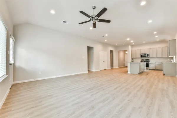 a view of a livingroom with a ceiling fan & kitchen space