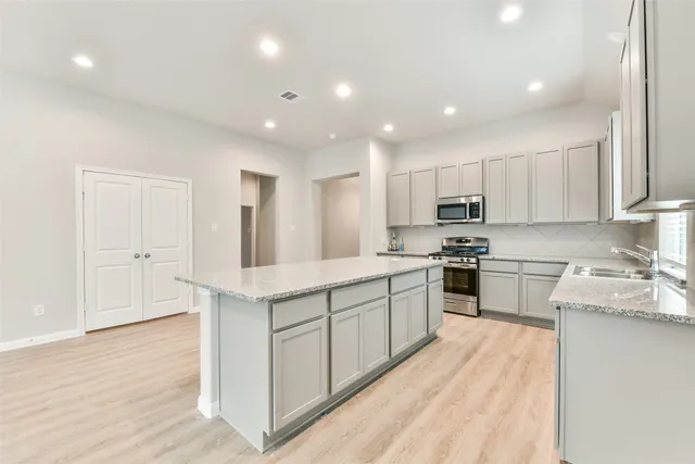 a kitchen with stainless steel appliances granite countertop a stove top oven a sink dishwasher and a refrigerator with wooden floor