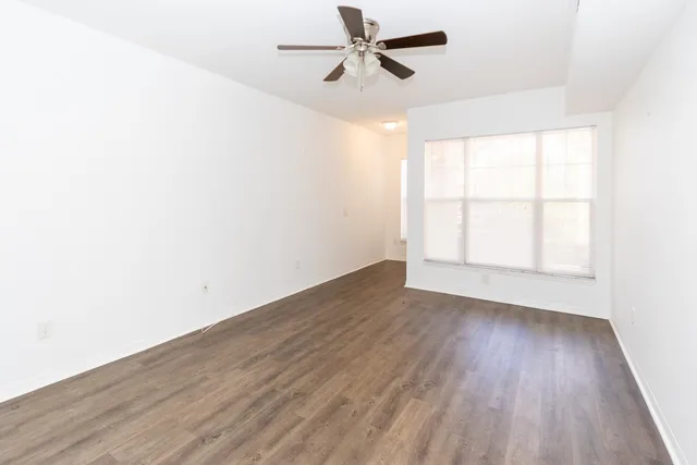 an empty room with wooden floor ceiling fan and windows