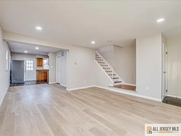 a view of an empty room with wooden floor and kitchen view