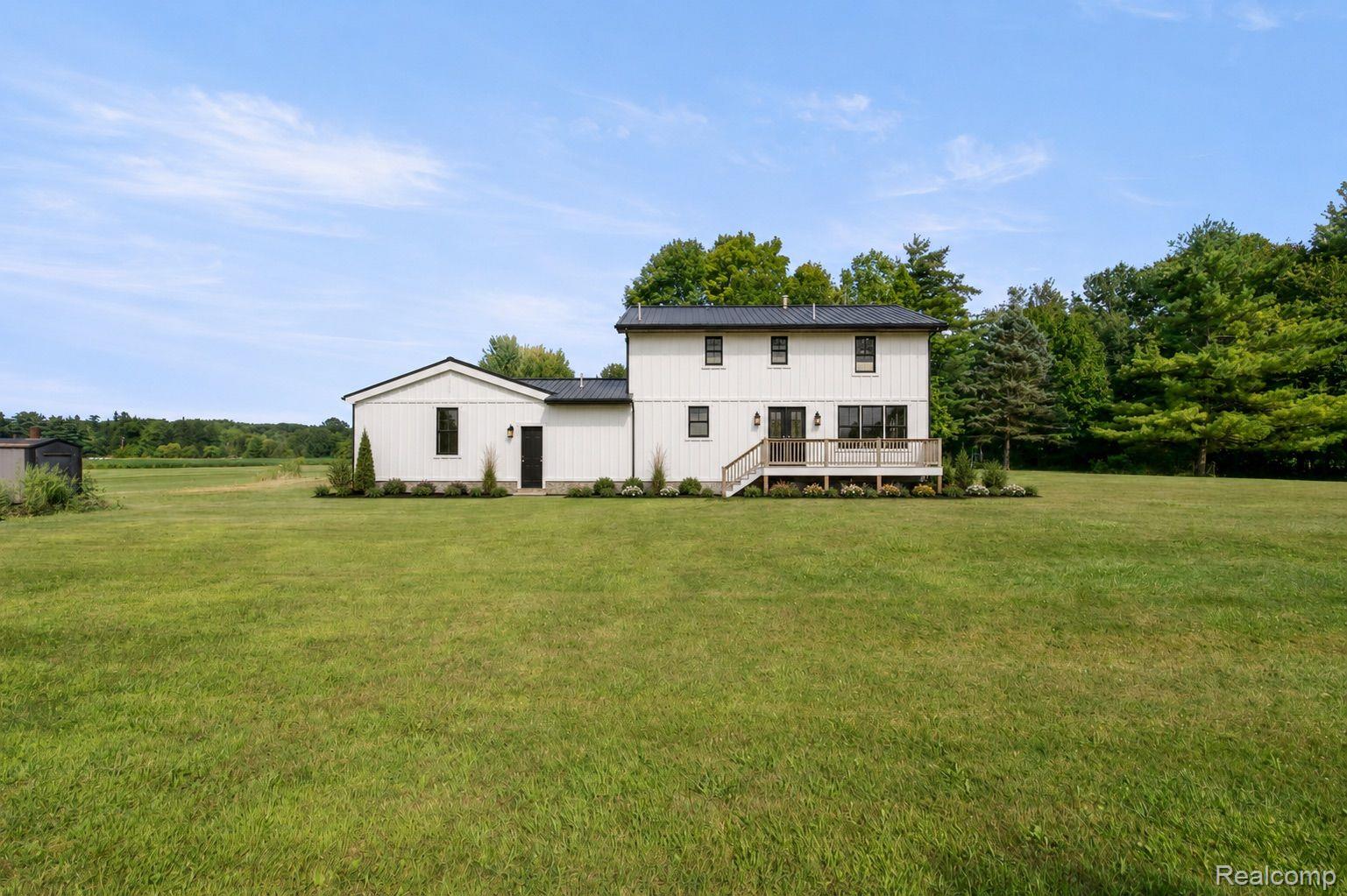 76565 McFadden Road Armada, MI 48005 - Photo 68 of 95 White vertical siding exterior with a dark metal roof, expansive lawn, rear deck, and mature trees bordering the property