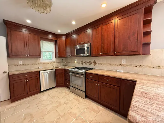 a kitchen with stainless steel appliances granite countertop wooden cabinets a sink and dishwasher a stove top oven with wooden floor