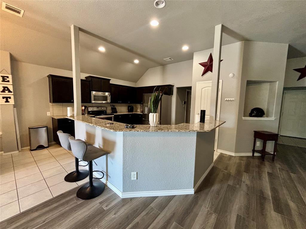 900 Grouse Road Glenn Heights, TX 75154 - Photo 5 of 13 a room with stainless steel appliances kitchen island granite countertop a refrigerator a stove a sink a dining table and chairs with wooden floor