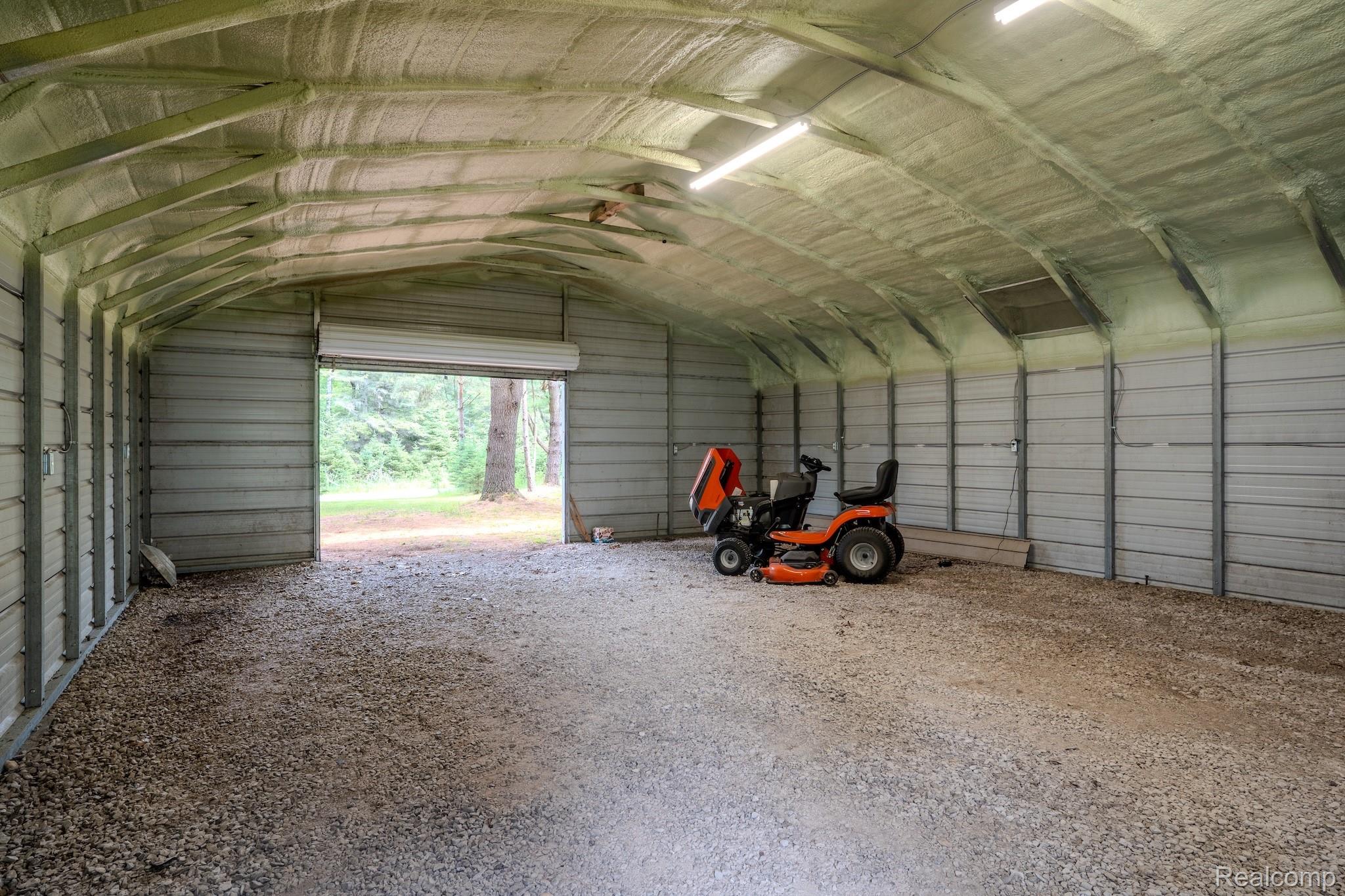 4350 Shrew Road Lincoln, MI 48742 - Photo 26 of 32 Spacious metal outbuilding featuring a corrugated steel exterior, roll-up door, insulated ceiling, strip lighting, and a gravel floor