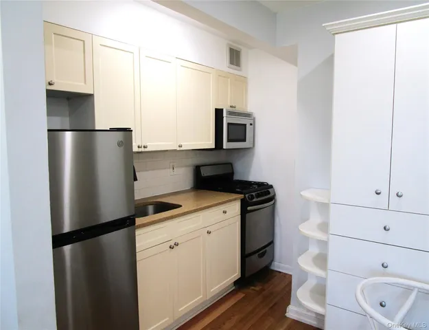 a kitchen with stainless steel appliances granite countertop a refrigerator a stove a sink and white cabinets with wooden floor