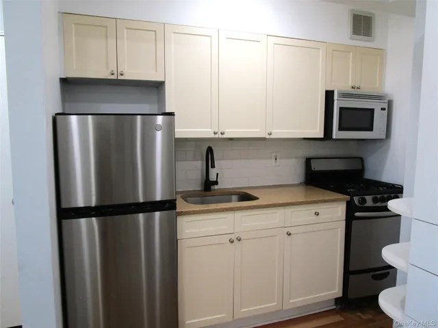 a kitchen with a refrigerator a stove a sink and white cabinets with wooden floor
