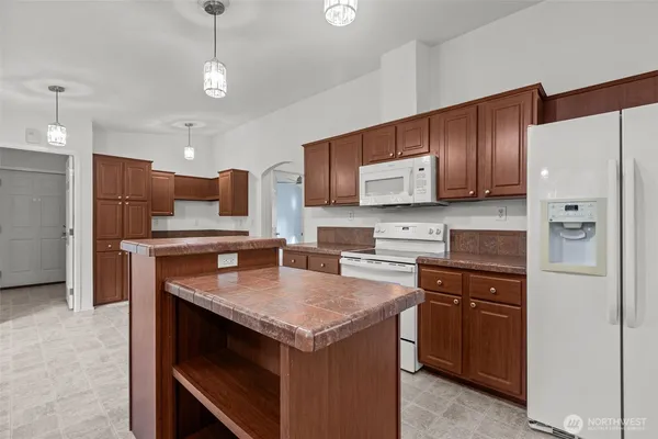 a kitchen with stainless steel appliances granite countertop a refrigerator a sink dishwasher a stove and white countertops with wooden floor