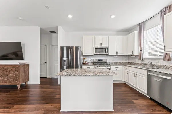 a kitchen with stainless steel appliances granite countertop a stove top oven a refrigerator a sink and dishwasher with wooden floor