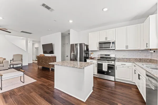 a kitchen with stainless steel appliances kitchen island granite countertop a stove top oven a sink dishwasher and a refrigerator with wooden floor
