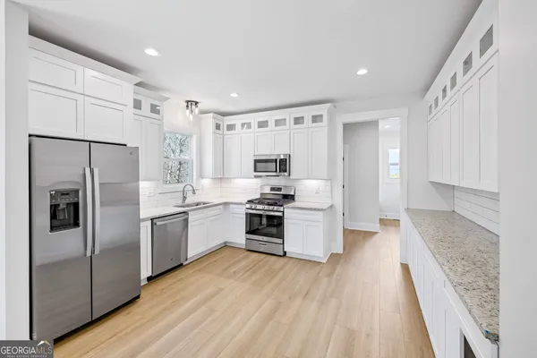 a kitchen with stainless steel appliances granite countertop a refrigerator oven a sink dishwasher and white cabinets with wooden floor