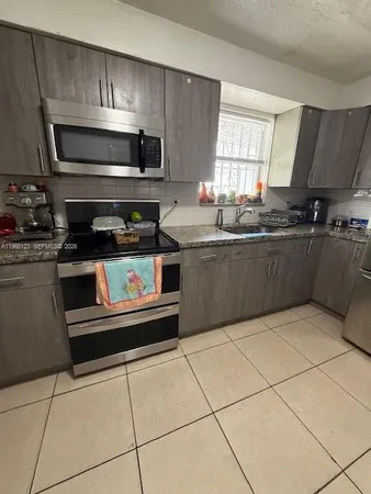 a kitchen with granite countertop a refrigerator a sink a stove a microwave and cabinets