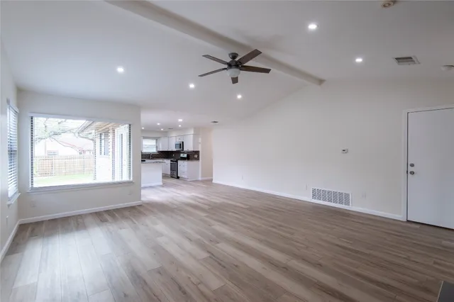 an empty room with wooden floor a ceiling fan and windows